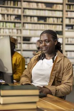 Black student uses desktop computer at library study table with stacked books 库存照片