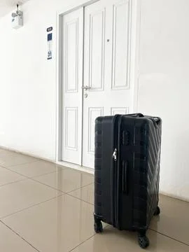 Black suitcase positioned in front of a closed white door with a number plate Photos