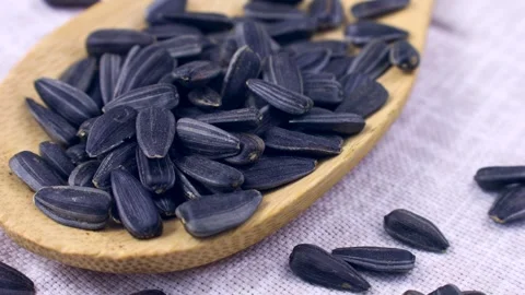 Black sunflower seeds falling down into a wooden spoon close up Stock Footage 268853638
