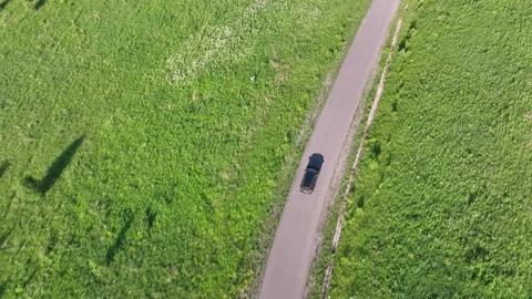 Black suv is driving on a road passing through a green meadow. Aerial view Stock Footage 300989094