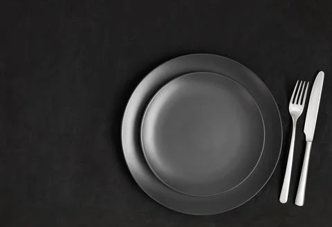 Black table setting. Empty black plate and silver cutlery on a dark concrete  Stockfoto's