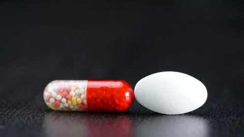 On the black table, a white tablet and an antibiotic in a capsule Stock Photos