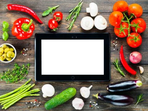 Black tablet pc with vegetables and herbs on wooden table Фото