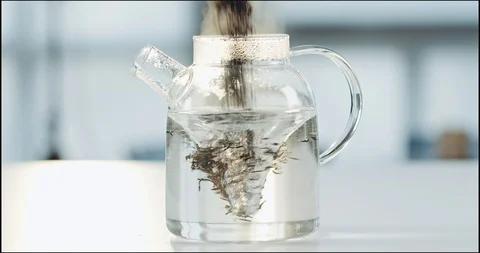 Black tea being dropped for brew into a glass teapot with hot water whirlpool Видео 101606119