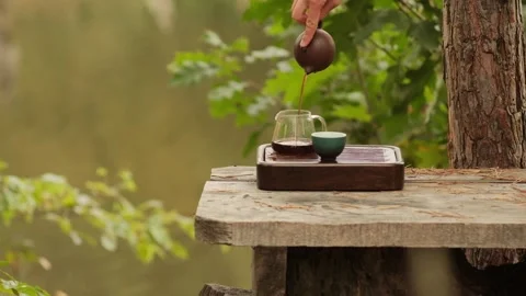 Black tea is being poured into tea ware on a tea tray, near a lake in a natural  Video stock 295279492