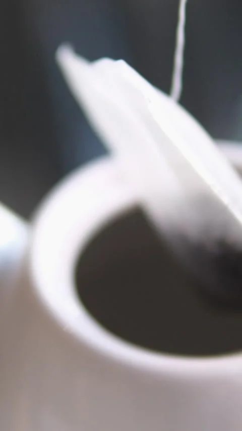 Black Tea Brewing in a White Mug. Tea Bag Comes Out Of A Cup On A Black Table In Stock Footage 302079689