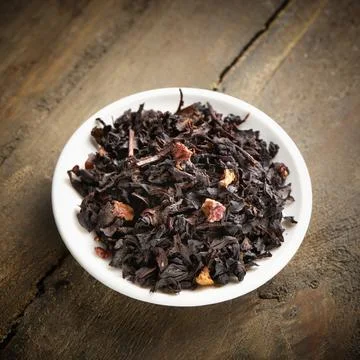 Black tea with red fruit in a small white plate on a wooden tabel Stock Photos