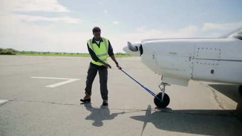Black Technician Pulling Small Aircraft across Sunny Airfield Stock Footage 310851034