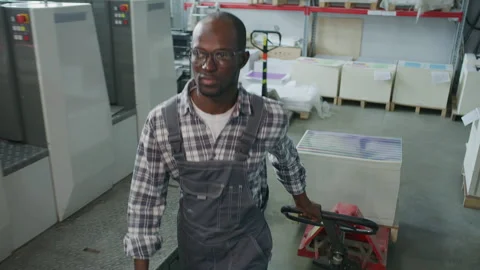 Black Technician Transporting Paper Pallets through Printing Factory Warehouse Stock Footage 335483548