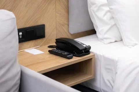 A black telephone and remote controller sit on a modern wooden bedside table Stock Photos