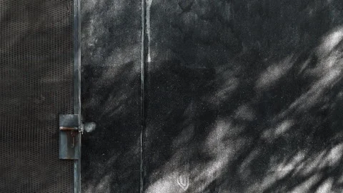 Black terrazzo stone wall beside industrial metal gate with moving tree shadows. Stock Footage 330149772