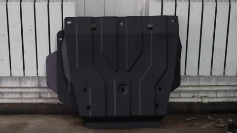 Black textured metal car engine skid plate against white radiator. 動画素材 343902204