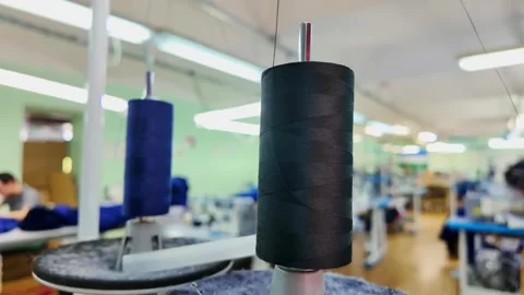Black thread spool closeup in textile workshop with blue spool behind, blurred Stock-Footage 346545939