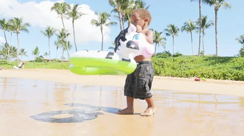 Black toddler playing in the ocean with an inflatable toy Vidéo 52919429