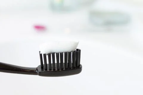Black toothbrush with toothpaste on blurred bathroom background. Stock Photos