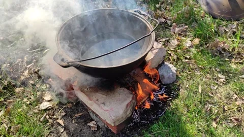 Black tourist pot stands on bricks over burning flame of campfire in spring Video stock 273801811