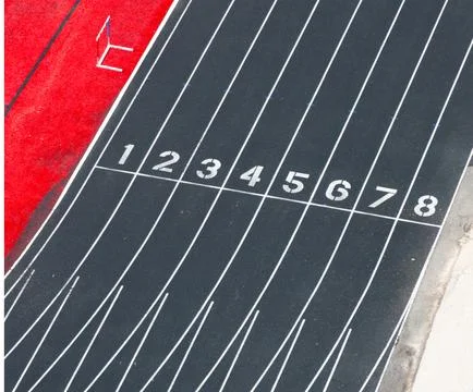 Black track surface with white lane markings and red starting blocks Stock Photos