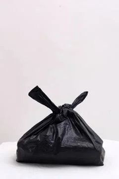 Black trash bag on white surface in plain setting Stock Photos