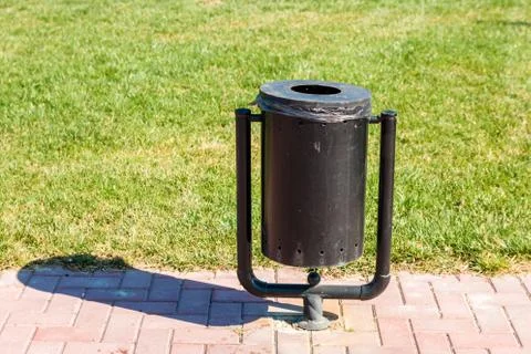 Black trash can on walking path by green lawn in park in spring Stock-Fotos
