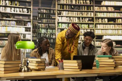 Black tutor leaning over shared study desk with laptop and open books Stock Photos