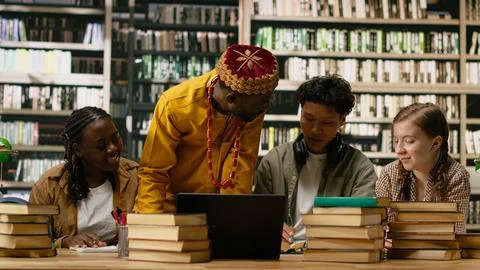 Black tutor leaning over shared study desk with laptop and open books Stock Photos