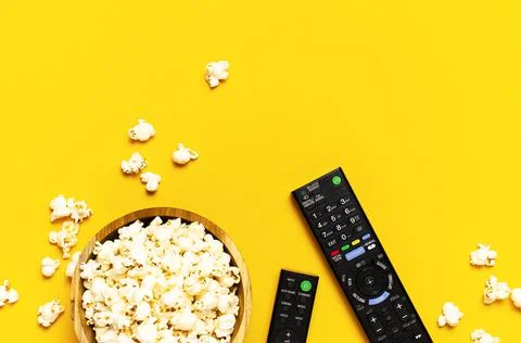 Black TV, audio remote control and popcorn on bright yellow background Stock Photos