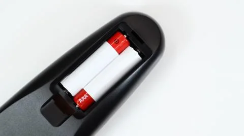 Black TV remote control with AAA alkaline batteries in red and white on a whi Stock Photos