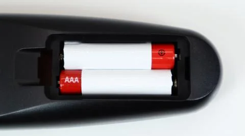 Black TV remote control with AAA alkaline batteries in red and white on a whi Stock Photos