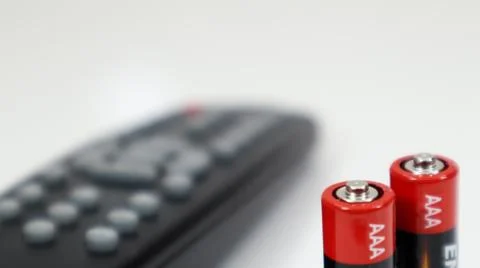 Black TV remote control with AAA alkaline batteries in red and white on a whi Stock Photos