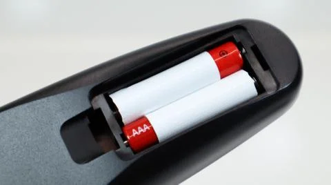 Black TV remote control with AAA alkaline batteries in red and white on a whi Stock-Fotos