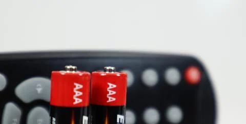 Black TV remote control with AAA alkaline batteries in red and white on a w.. Stockfoto's