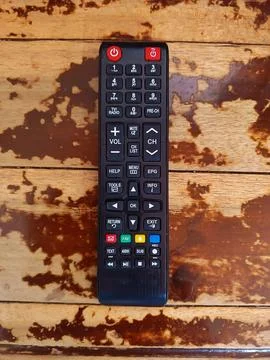 Black TV remote control lying on a textured, glossy wooden table. Stock Photos