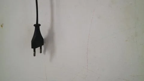 Black two pin power cable plug hanging against a white wall representing en.. Stock-Fotos