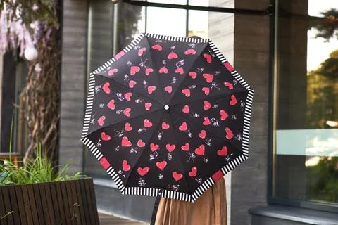 Black umbrella with red heart pattern held by person outside modern buildin.. 스톡 사진