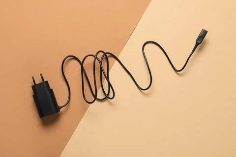 Black USB charger with coiled cable on dual-tone beige and brown background,  Stock Photos