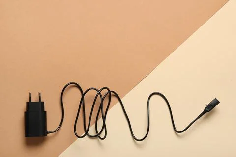 Black USB charger with coiled cable on dual-tone beige background, power supp Stock Photos