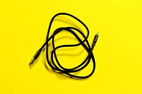 Black usb iPhone charging cable, coiled in a ring, on a yellow background. Stock Photos