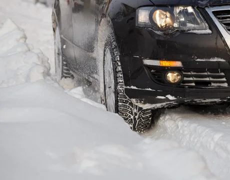 Black vehicle moving through the deep snow skidding, car's wheel spin and spew Фото