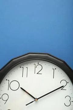 Black wall clock on the blue background. Vertical photo. Stock Photos