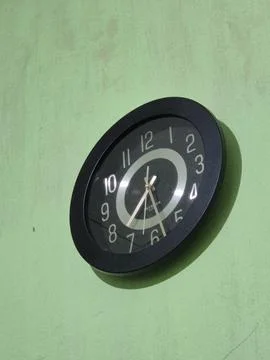 A black wall clock on a light green wall Фото