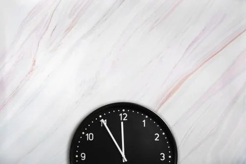 Black wall clock on marble texture with natural pattern. Office clock on marble Stock Photos