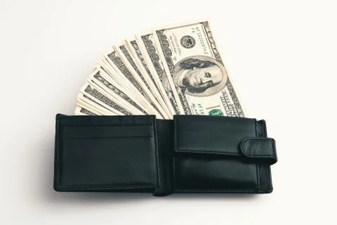 A black wallet with dollars in it on a white background. Stock Photos