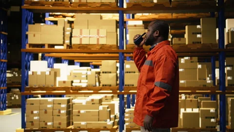 Black warehouse operator using portable walkie-talkie radio in distribution hub Stock Footage 332908988
