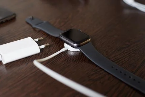 The black watch is lying on a dark table next to the adapter with a wire, so  Stock Photos