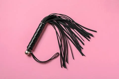 Black whip on pink background, top view. Sexual role play accessory Stock Photos