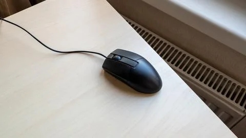 Black wired computer mouse on a light wood desk, ready for use in office work 库存照片