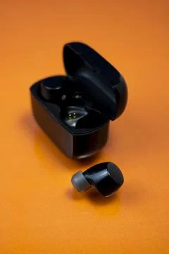 Black Wireless Earbuds and Case on Bright Orange Background Stock-Fotos