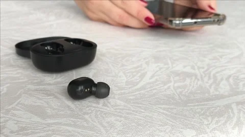 Black wireless headphones on the table, in the background a woman holding a Stock Footage 318206277