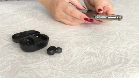 Black wireless headphones on the table, in the background a woman holding a Stock Footage 318206304