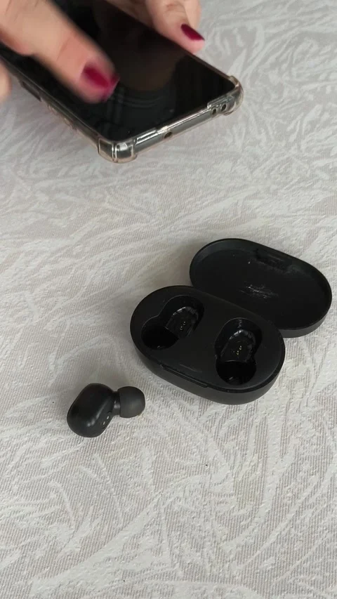 Black wireless headphones on the table, in the background a woman holding a Stock Footage 318206354